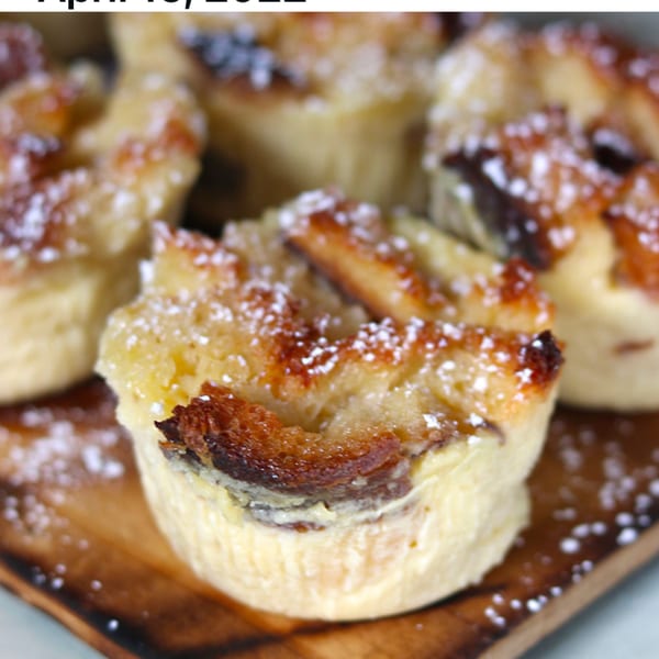 Close-up of golden-brown bread pudding muffins dusted with powdered sugar on a wooden board.