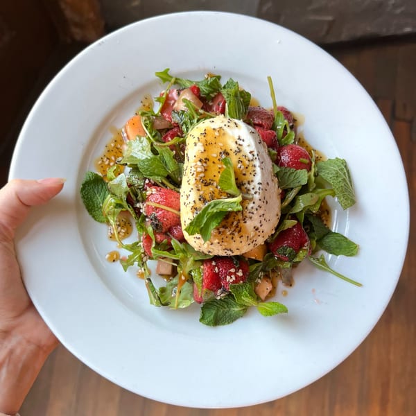 A fresh salad with burrata cheese, strawberries, arugula, mint, and a poppy seed dressing.