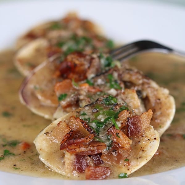 Clams in a rich sauce, topped with crispy bacon bits and fresh parsley, with a fork.