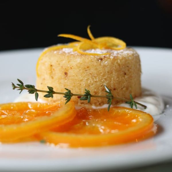 Orange cake with candied orange slices, powdered sugar, and a sprig of thyme.