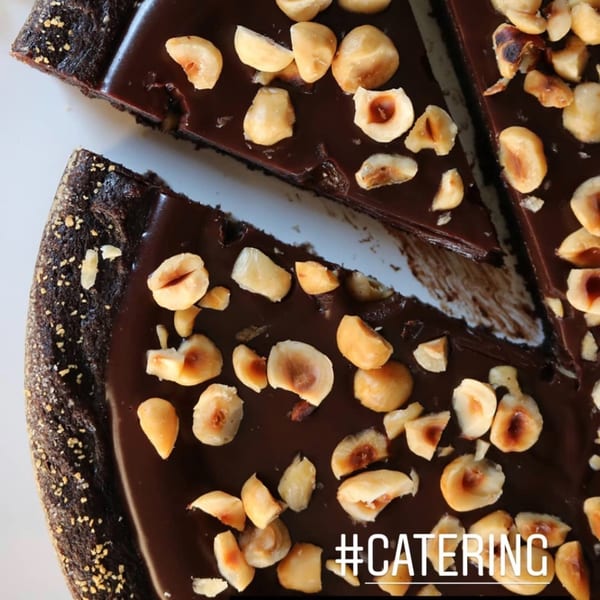 Close-up of a rich chocolate tart with a slice removed, topped with roasted hazelnuts.