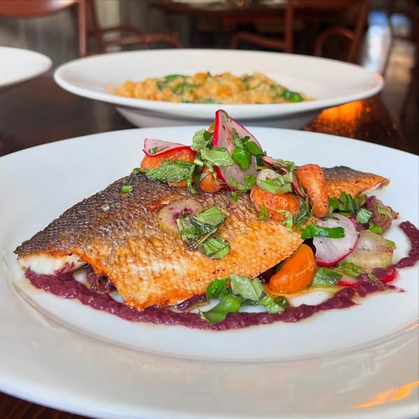 Crispy-skinned fish with radishes, herbs, and orange segments, drizzled with a purple sauce.