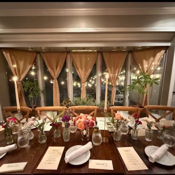 A long dining table set for a formal dinner with floral centerpieces and candles, illuminated by string lights.