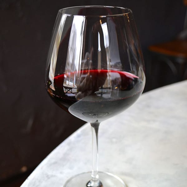A glass of red wine sits on a white marble table with a dark background.
