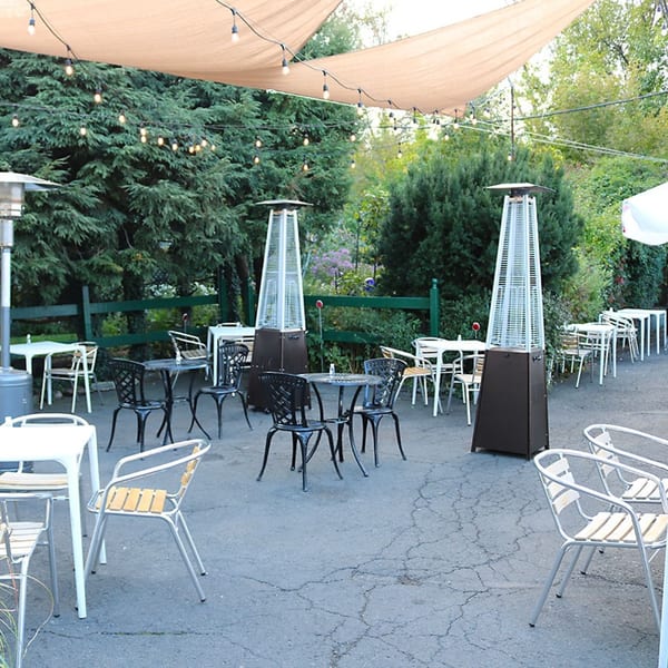 Outdoor patio dining area with various tables and chairs, string lights, and two tall patio heaters.