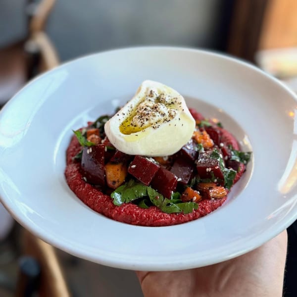A vibrant beet salad with burrata, olive oil, and spices, served on a white plate.