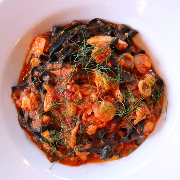 Black squid ink pasta with shrimp and calamari in a rich red tomato sauce, garnished with dill.