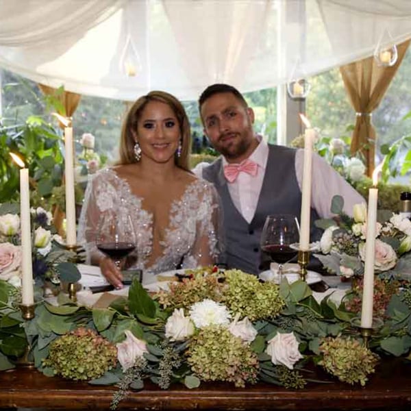 A couple in formal attire sits at a beautifully decorated table with flowers, candles, and wine.