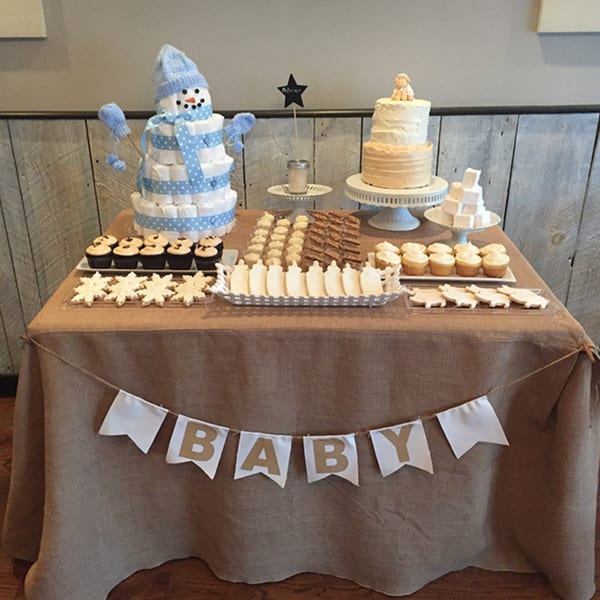 A baby shower dessert table with a diaper snowman, cake, cupcakes, and themed cookies.