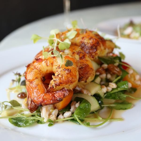 Grilled shrimp with microgreens, cucumber, and barley on a white plate.