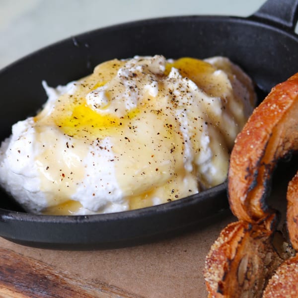 Whipped feta with honey and black pepper in a black skillet, served with toasted bread.