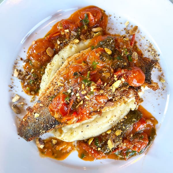 Pan-seared fish fillet with crispy skin, topped with tomato sauce, herbs, and crushed nuts.