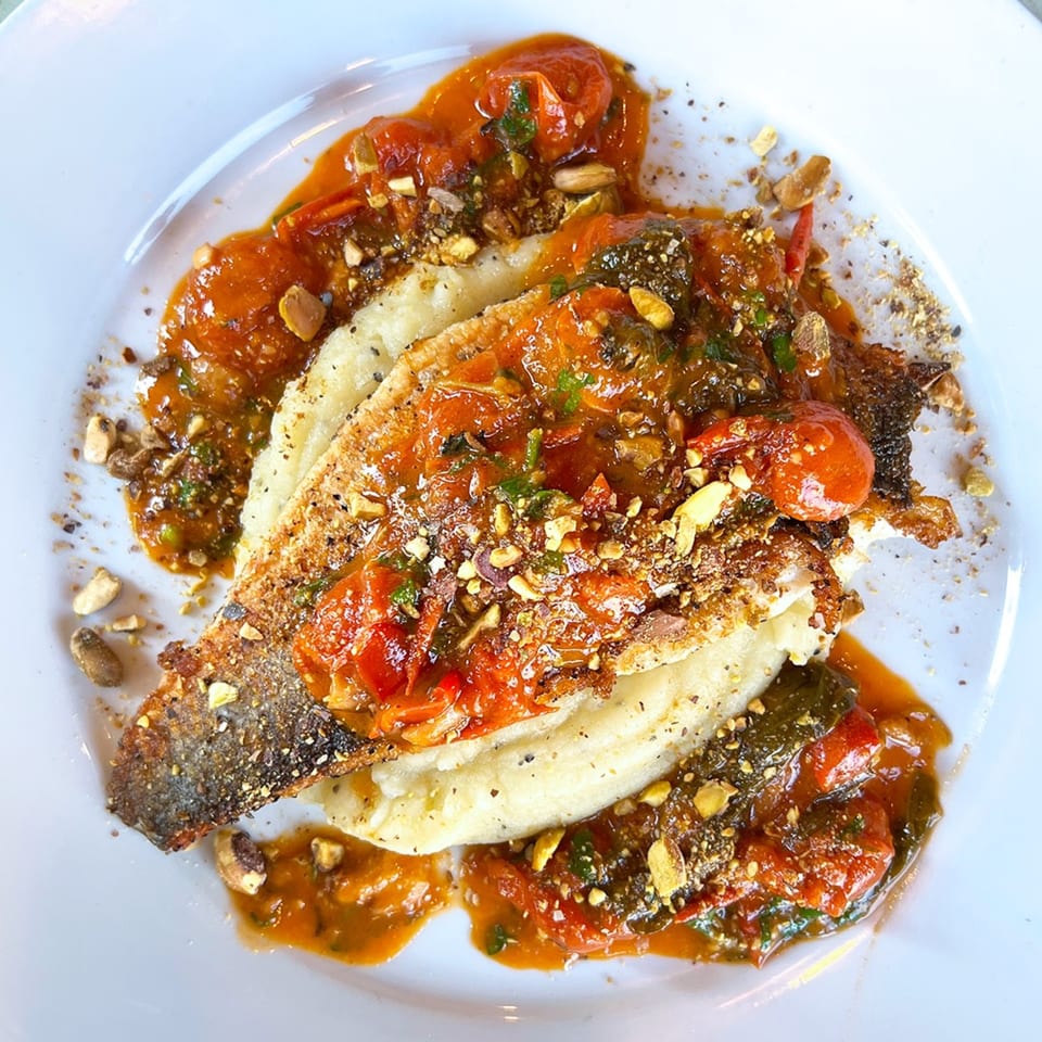 Pan-seared fish fillet with crispy skin, topped with tomato sauce, herbs, and crushed nuts.