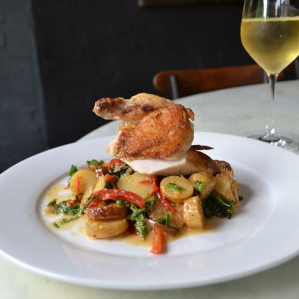 Roasted chicken with potatoes, red peppers, and greens, served with a glass of white wine.