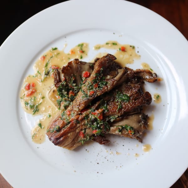 Grilled mushrooms with a creamy sauce, green herbs, and red peppers on a white plate.