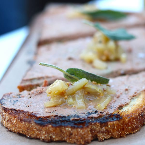 Close-up of pâté on toasted bread, topped with pear chutney and a sage leaf.