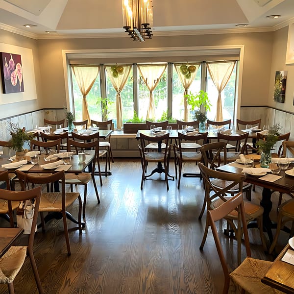 An empty restaurant dining room with wooden tables and chairs, set with white napkins and glasses.