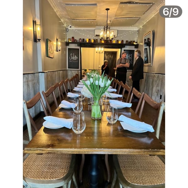 Long dining table set with white tulips, plates, and glasses, with two men conversing in the background.