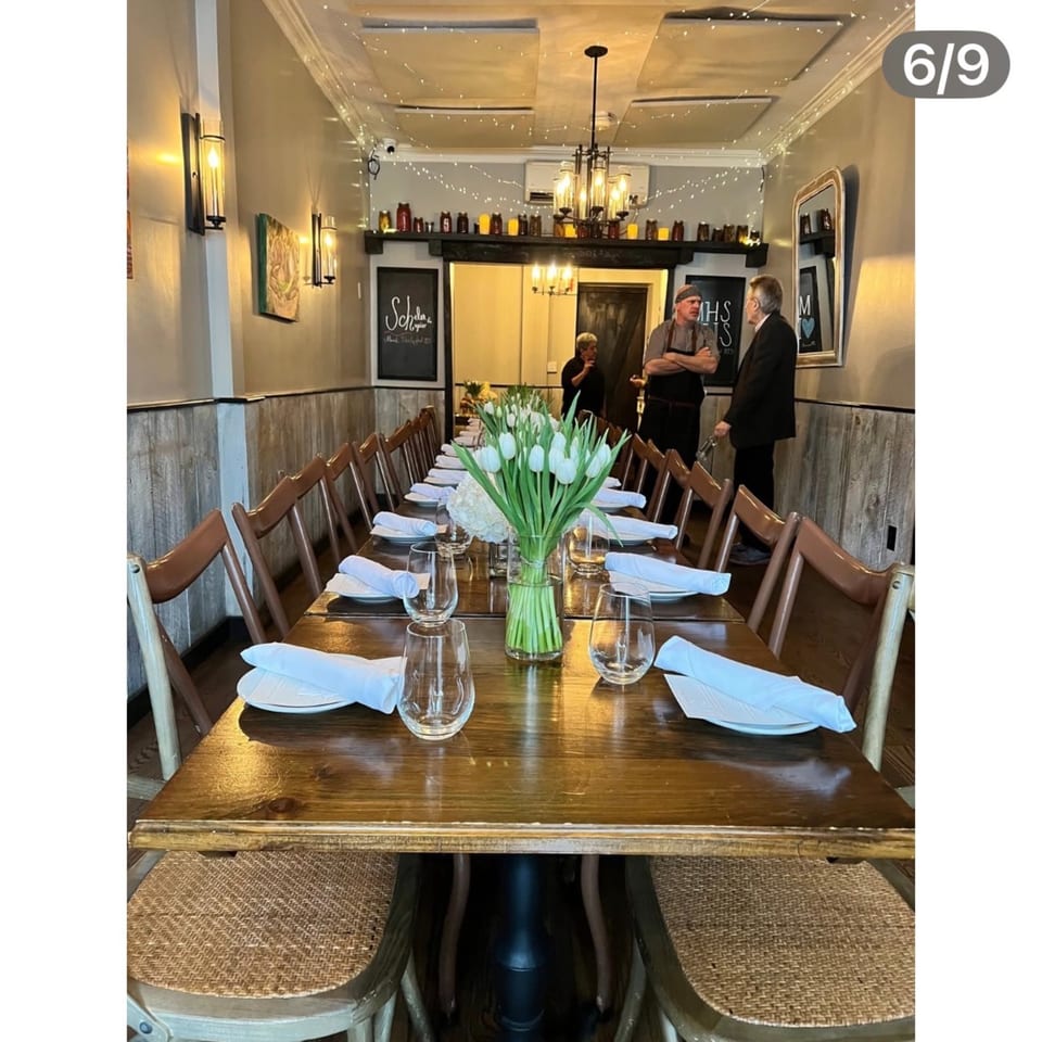 Long dining table set with white tulips, plates, and glasses, with two men conversing in the background.