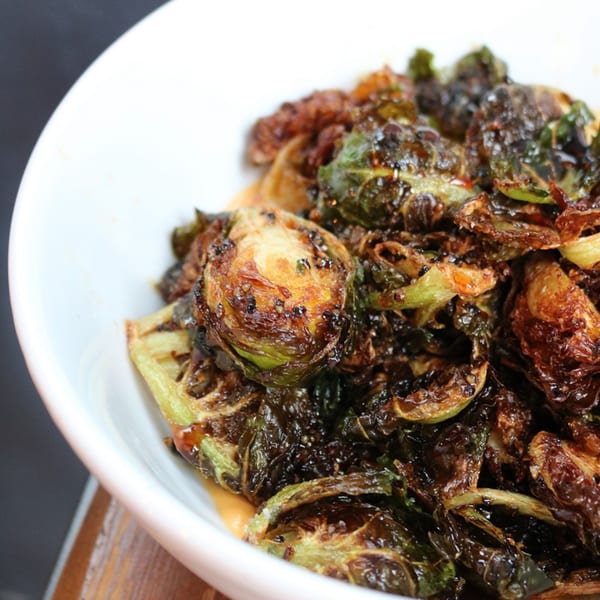 Close-up of crispy, dark brown roasted Brussels sprouts in a white bowl with a creamy sauce.