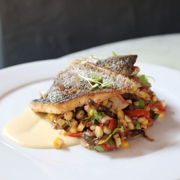Pan-seared fish with crispy skin, served over a colorful corn and vegetable medley with a creamy sauce.